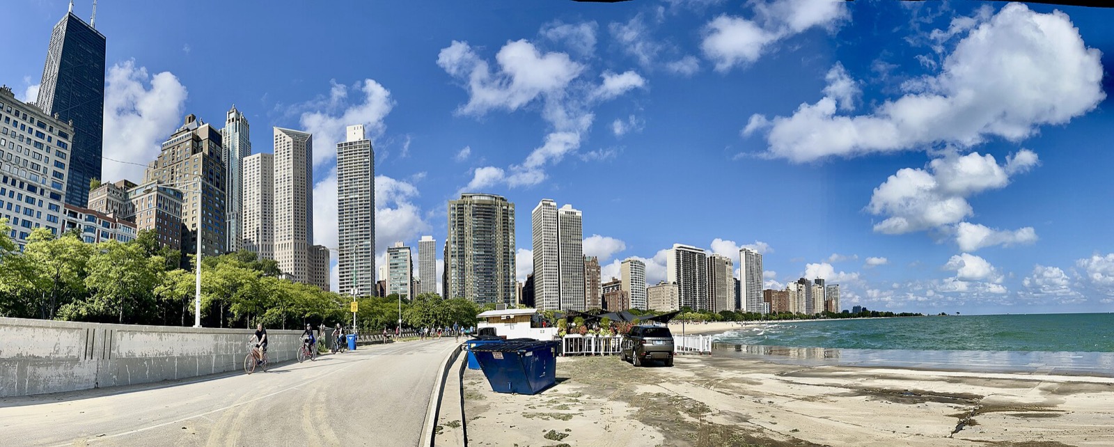 Cyclists on the Lakefront Trail beside Lake Michigan under a blue sky, with lakefront towers behind