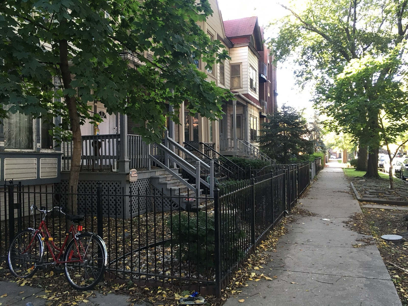 A red bicycle leaning against an iron fence on a residential Chicago street