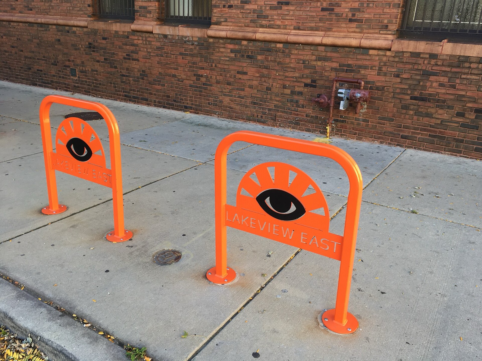 Two orange bike racks on a Chicago sidewalk in front of a brick wall
