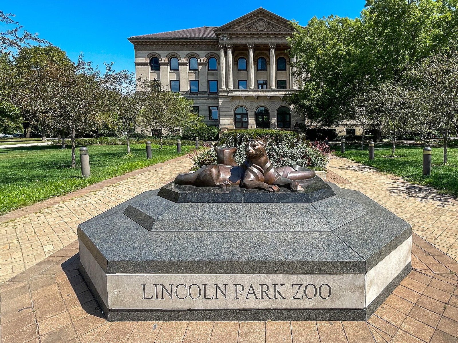 The Lincoln Park Zoo entrance sign on a granite base with bronze big cats, and the zoo building behind