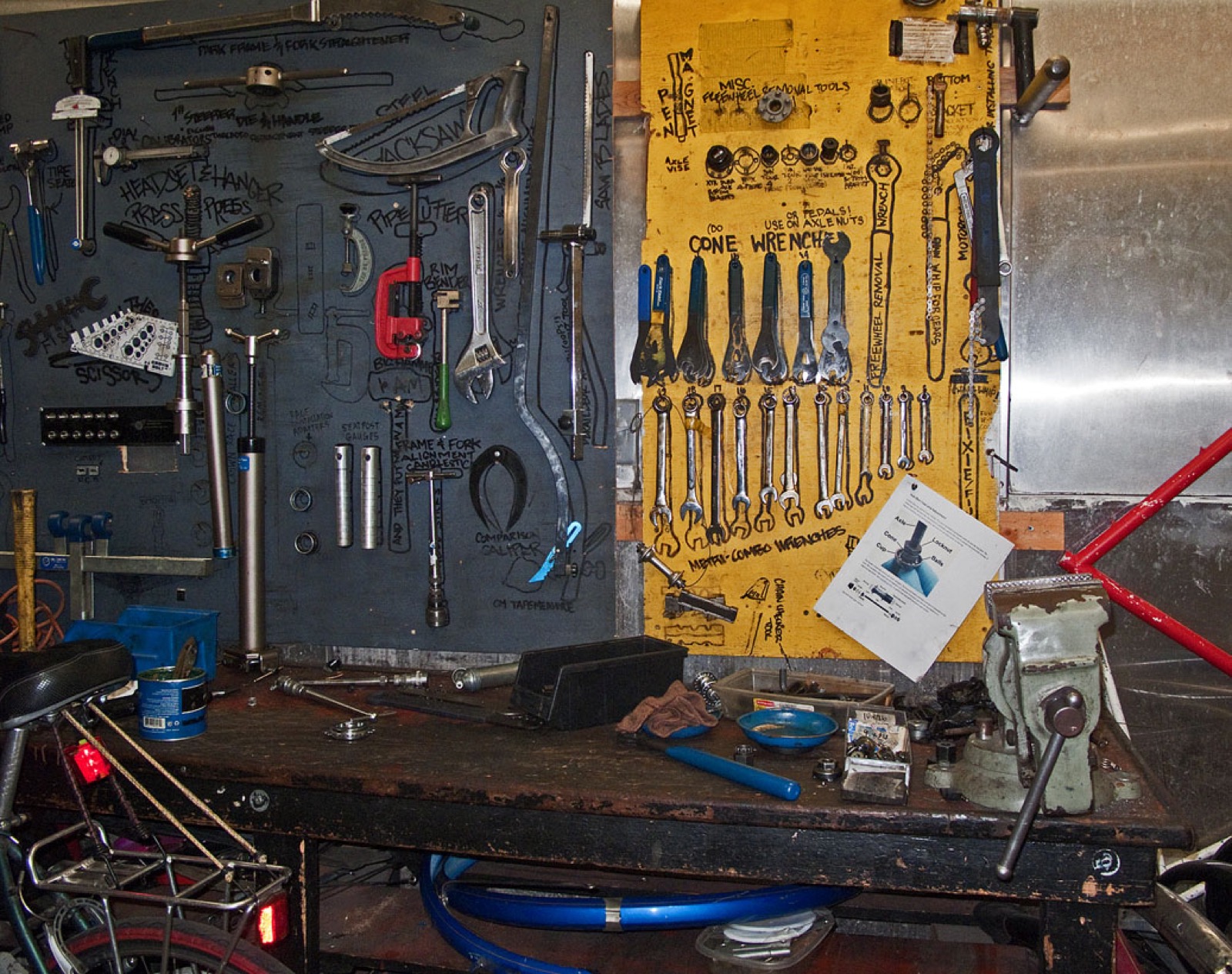 A bike workshop wall of hand tools and wrenches above a worn repair bench with a vise