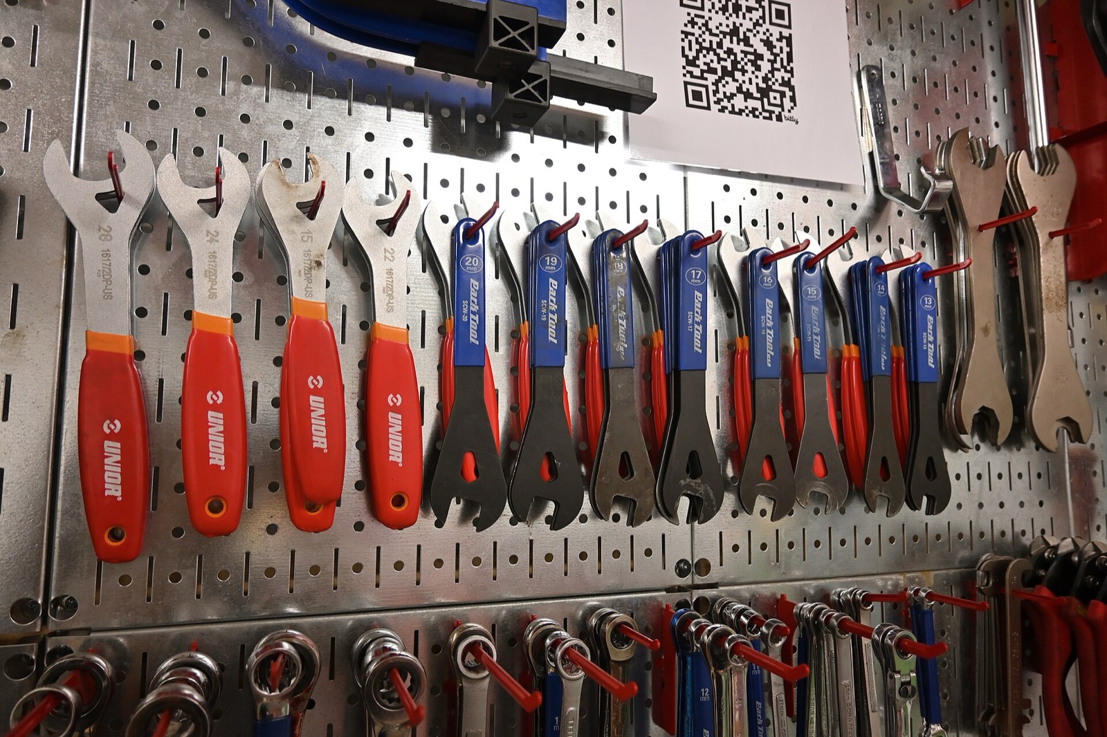 Rows of cone wrenches with red and blue handles hanging on a pegboard wall in a community bike shop
