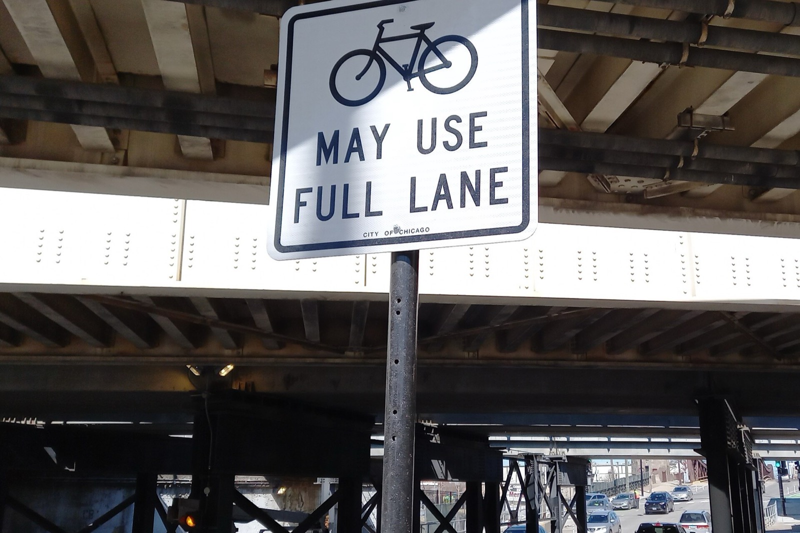 A Chicago sign reading Bikes May Use Full Lane mounted beneath an elevated structure