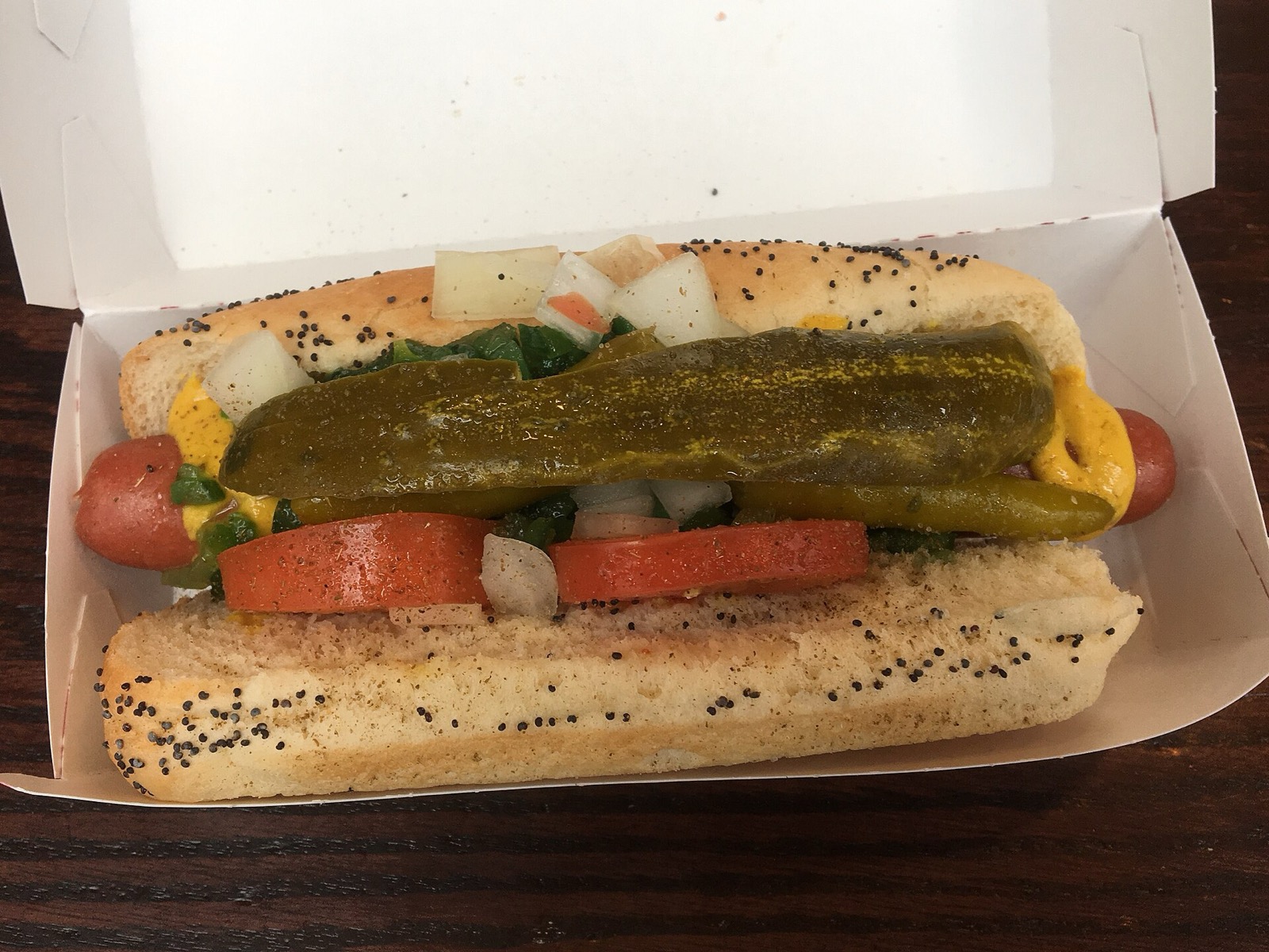 A Chicago-style hot dog with mustard, onion, relish, tomato, pickle spear and sport peppers on a poppy seed bun