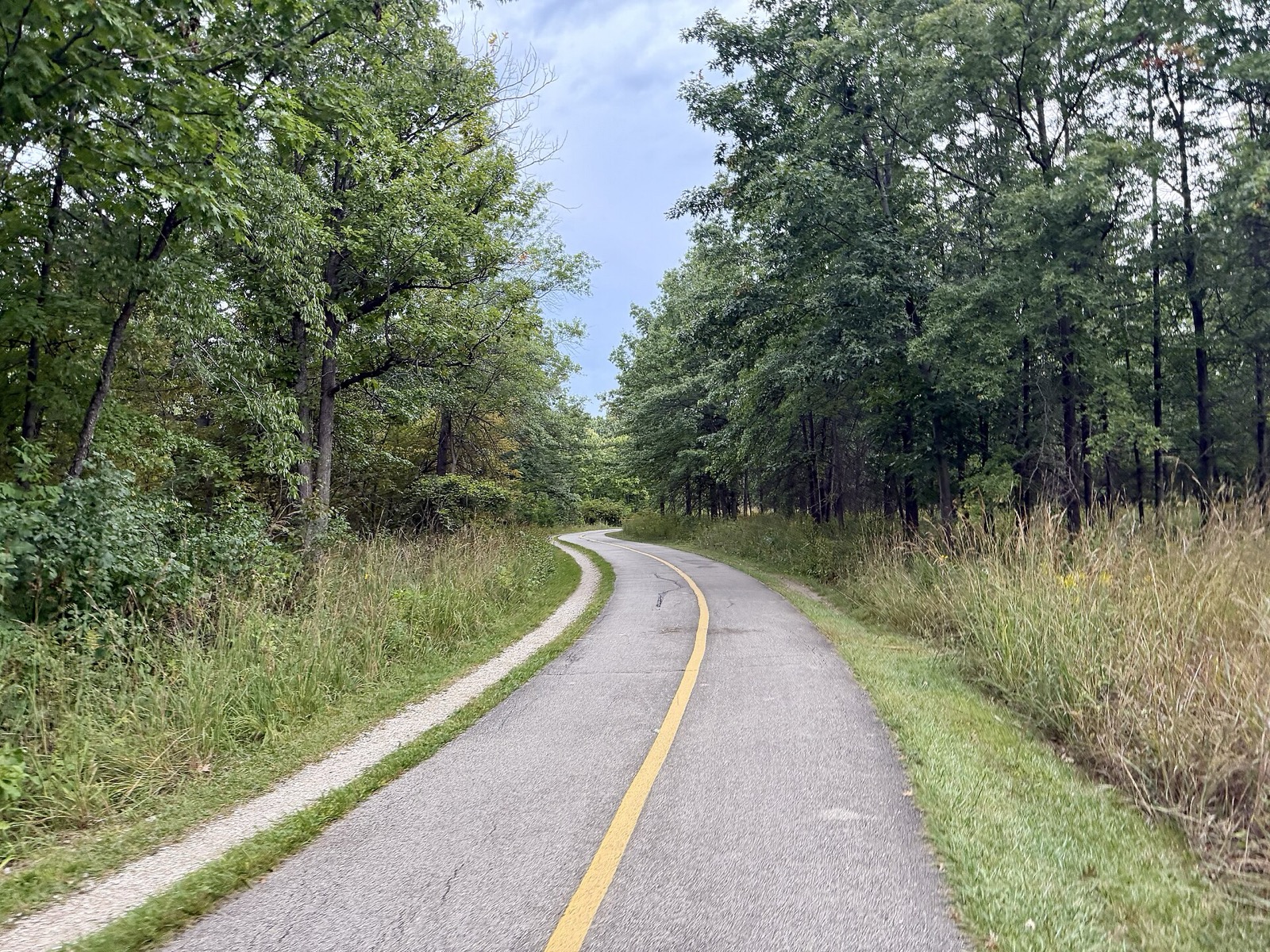 Paved North Branch Trail curving between woods and prairie grass