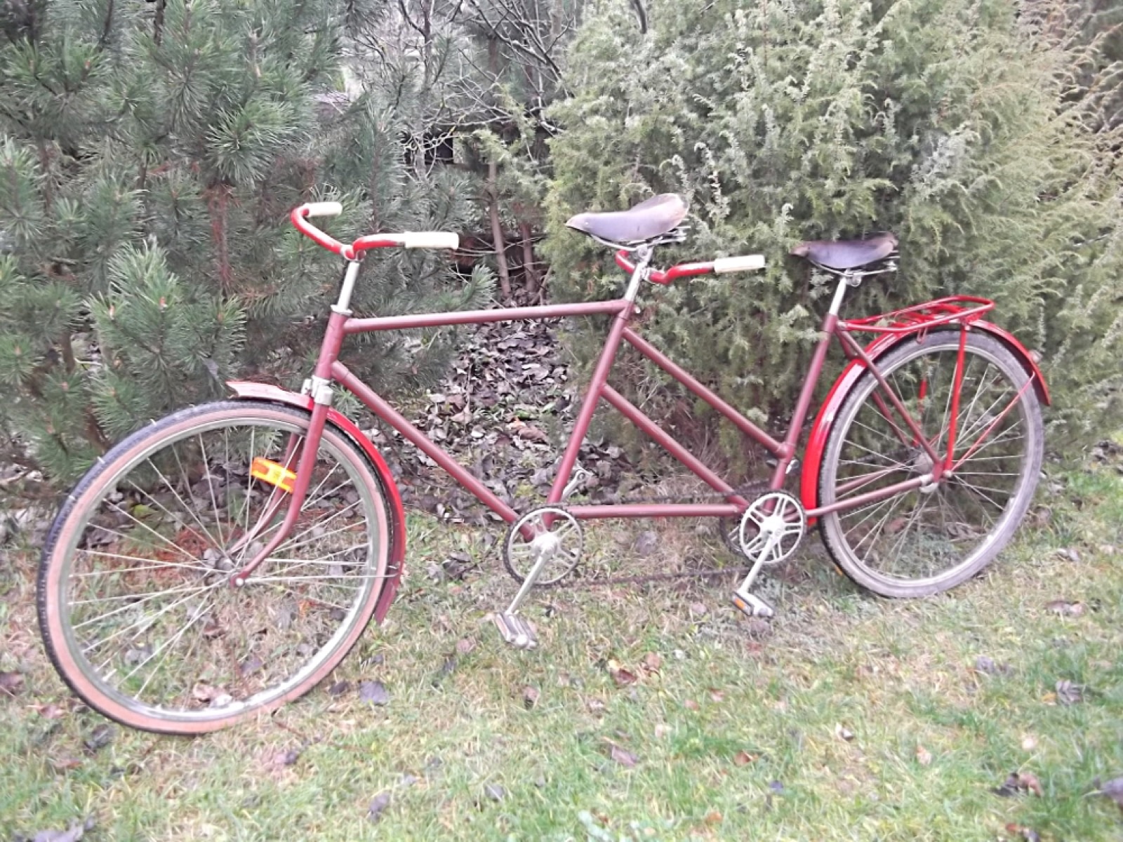 A red tandem bicycle with two seats standing on grass